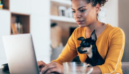 Young afro-american woman sitting with her pet dog and using laptop at home